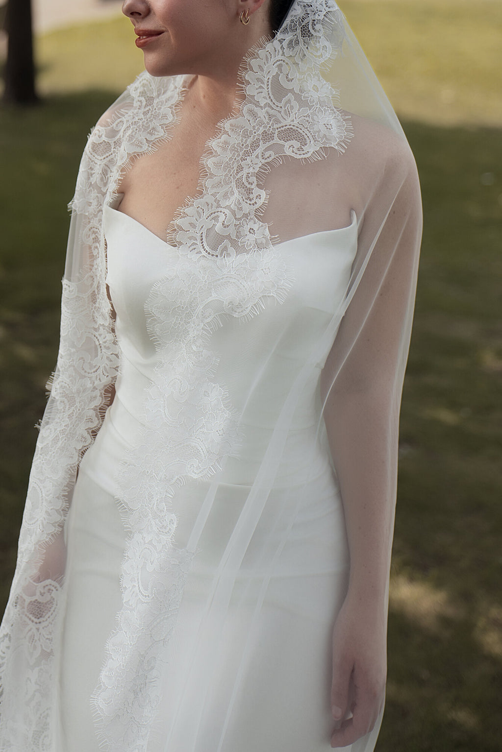 Detail of The Close Up lace mantilla veil outdoors, scalloped lace border running down the front edge across the bodice