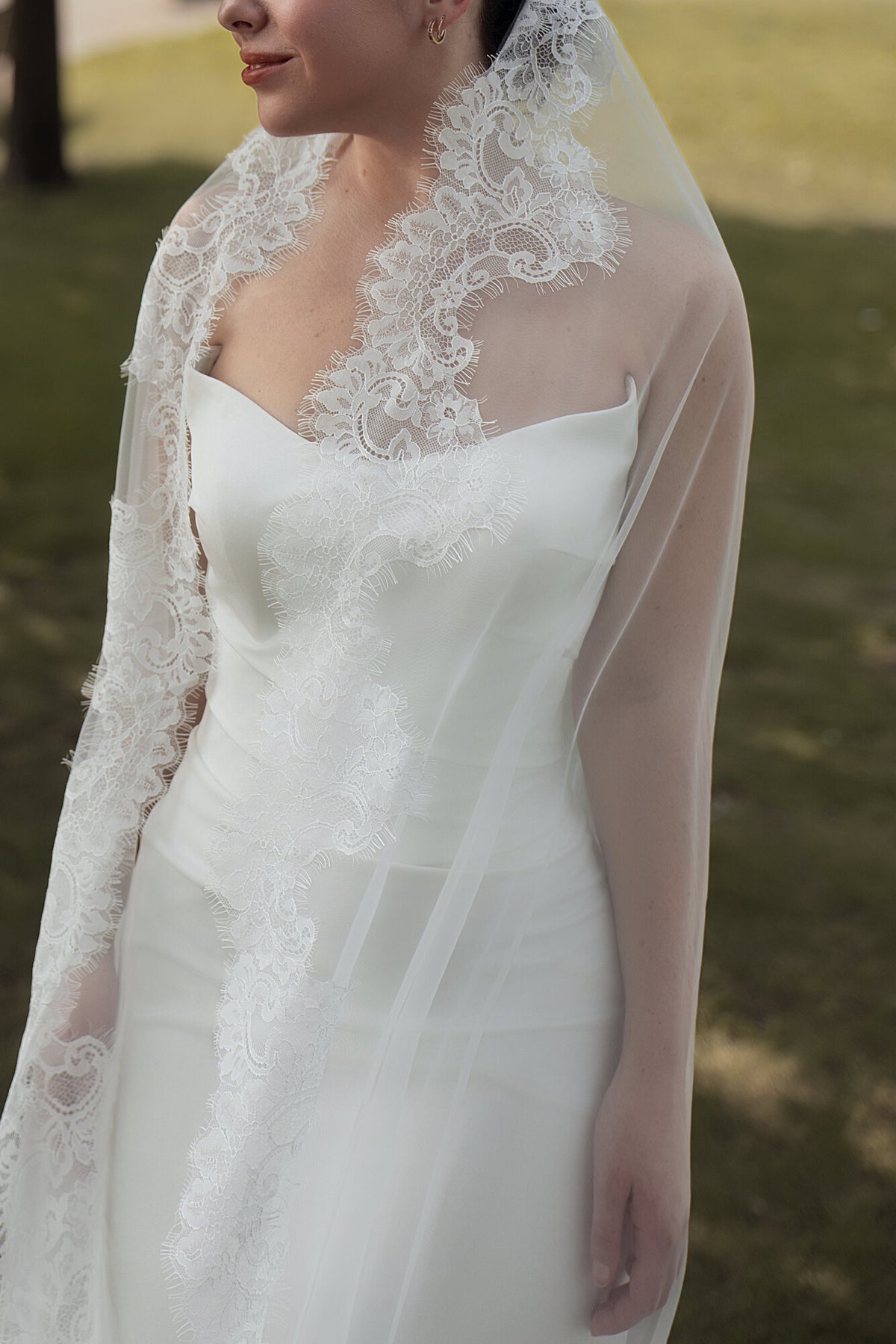 Detail of The Close Up lace mantilla veil outdoors, scalloped lace border running down the front edge across the bodice