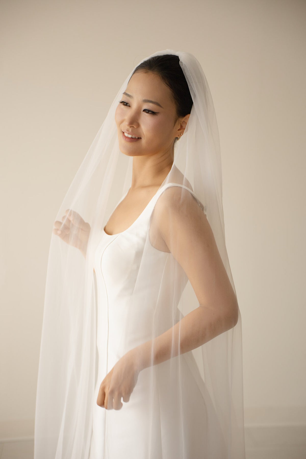 Bride in a white satin gown wearing The Barely There single tier cathedral veil draped forward over one shoulder, photographed against a soft neutral backdrop