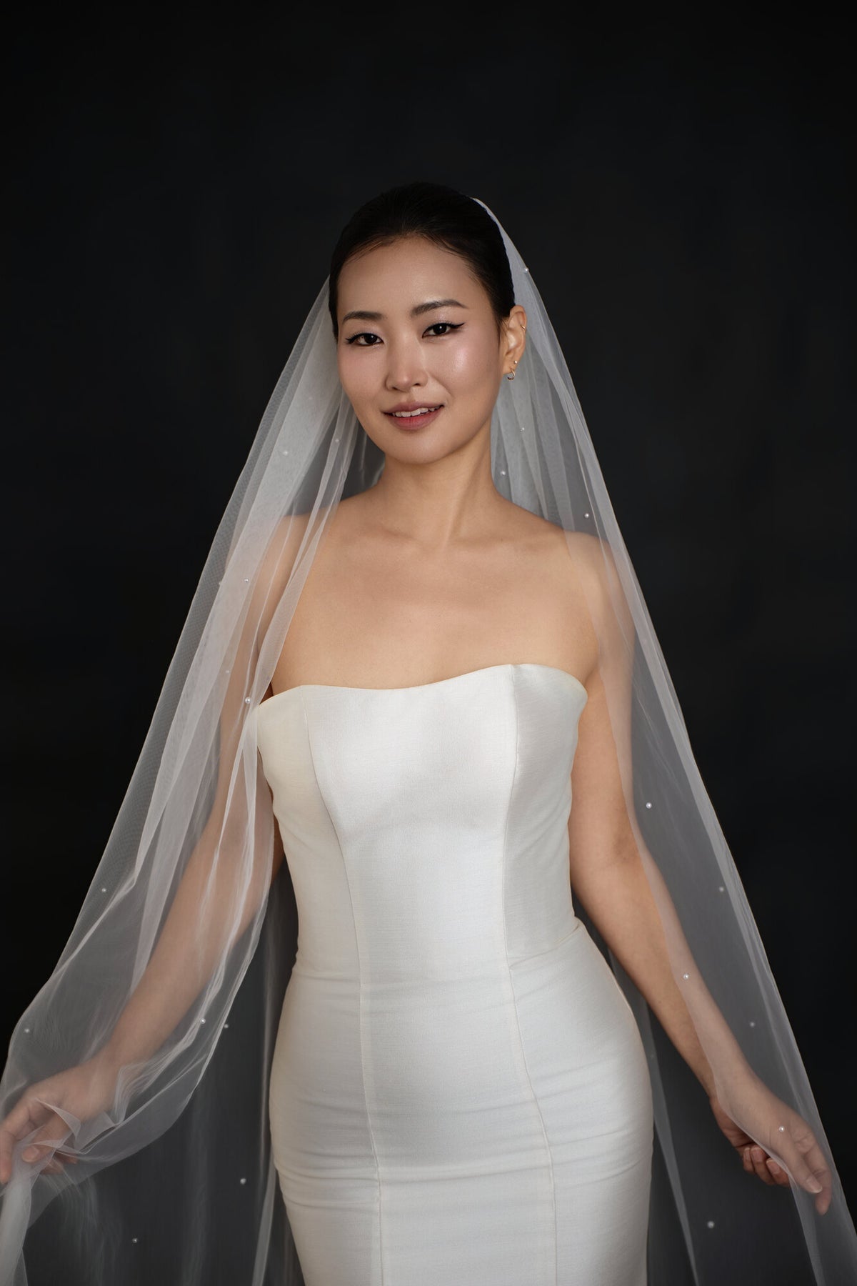 Front view of The Soft Focus cathedral veil with pearls scattered across the tulle, worn over a strapless satin gown
