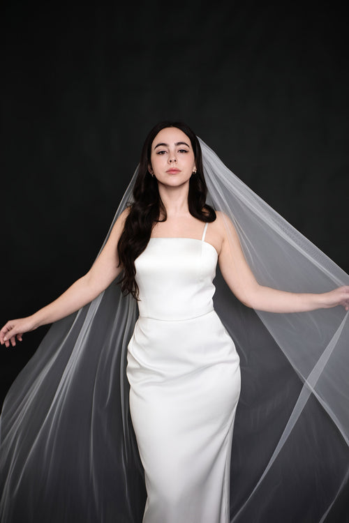 Bride holding The Barely There cathedral veil open with both arms extended, showing the width of the plain cut edge tulle