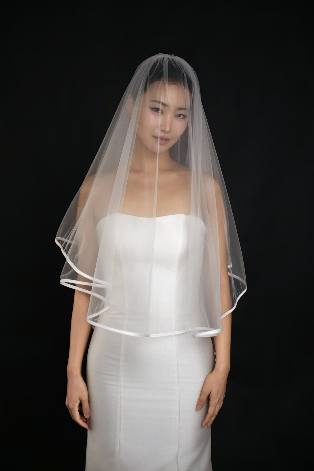 The Clean Line veil worn with the blusher layer forward over the face, satin ribbon edge visible at the hem