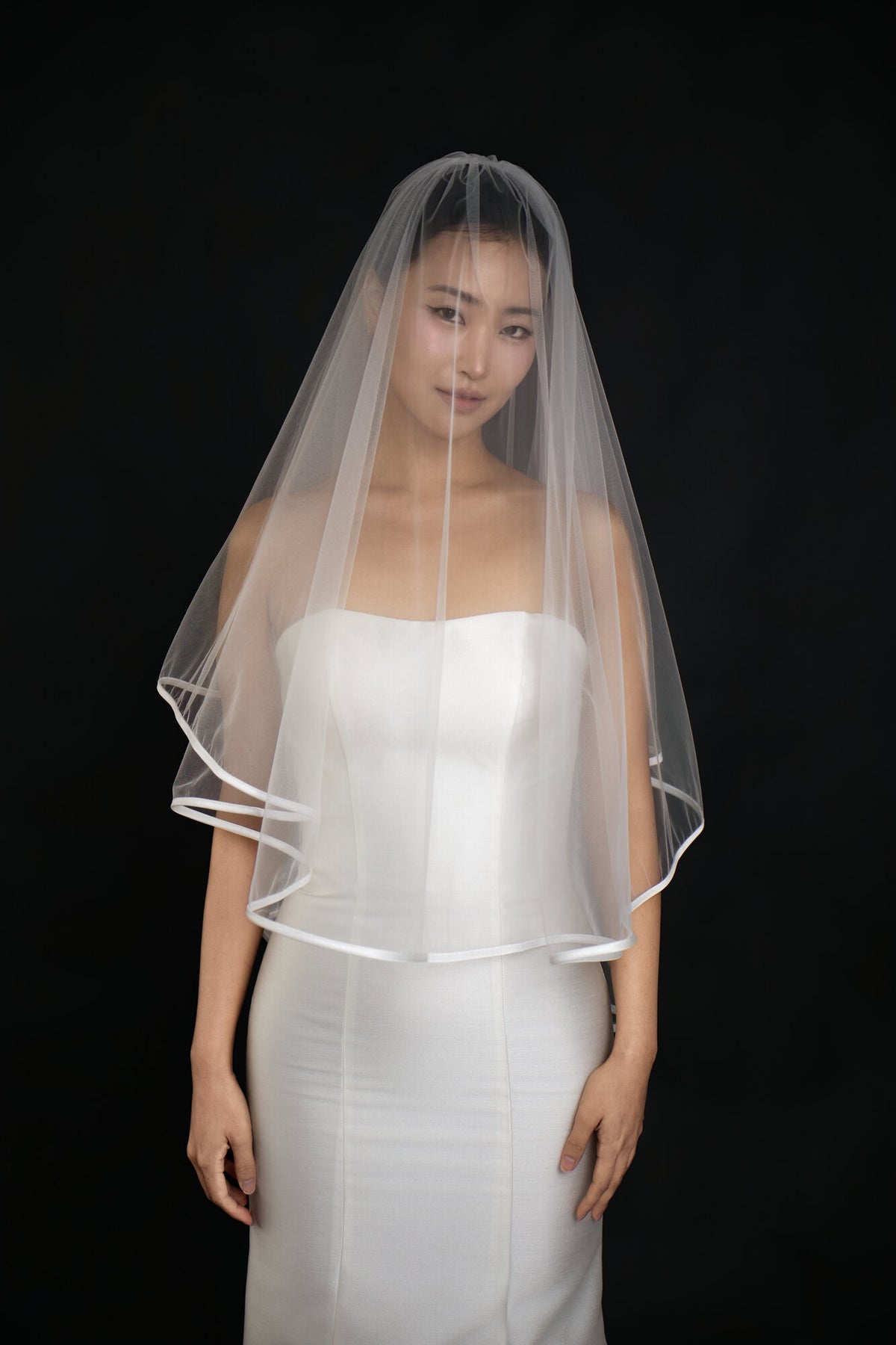 The Clean Line veil worn with the blusher layer forward over the face, satin ribbon edge visible at the hem