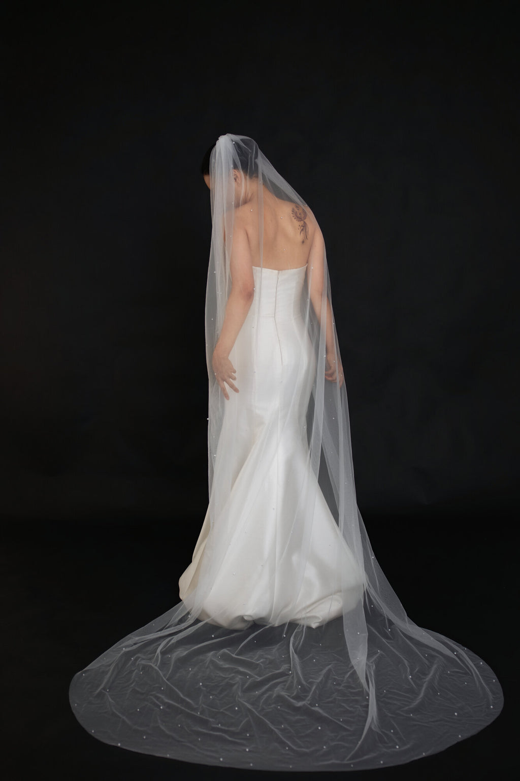 Back view of The Soft Focus cathedral veil spread across the floor, scattered pearls visible along the full length