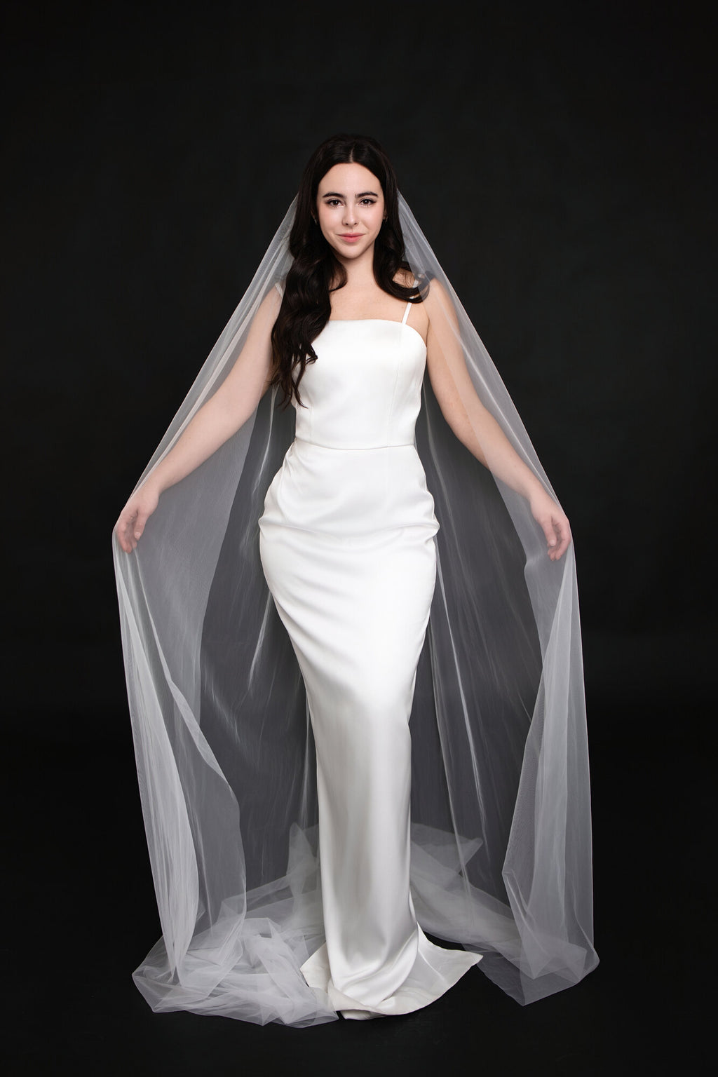 The Barely There cathedral veil framing both sides of a strapless white satin gown, front view showing the veil falling past the hem