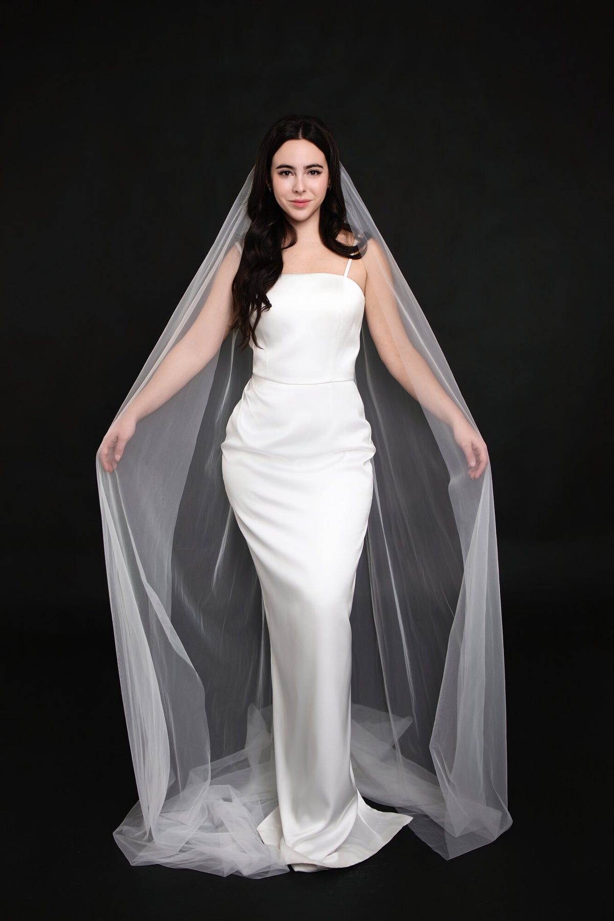 The Barely There cathedral veil framing both sides of a strapless white satin gown, front view showing the veil falling past the hem